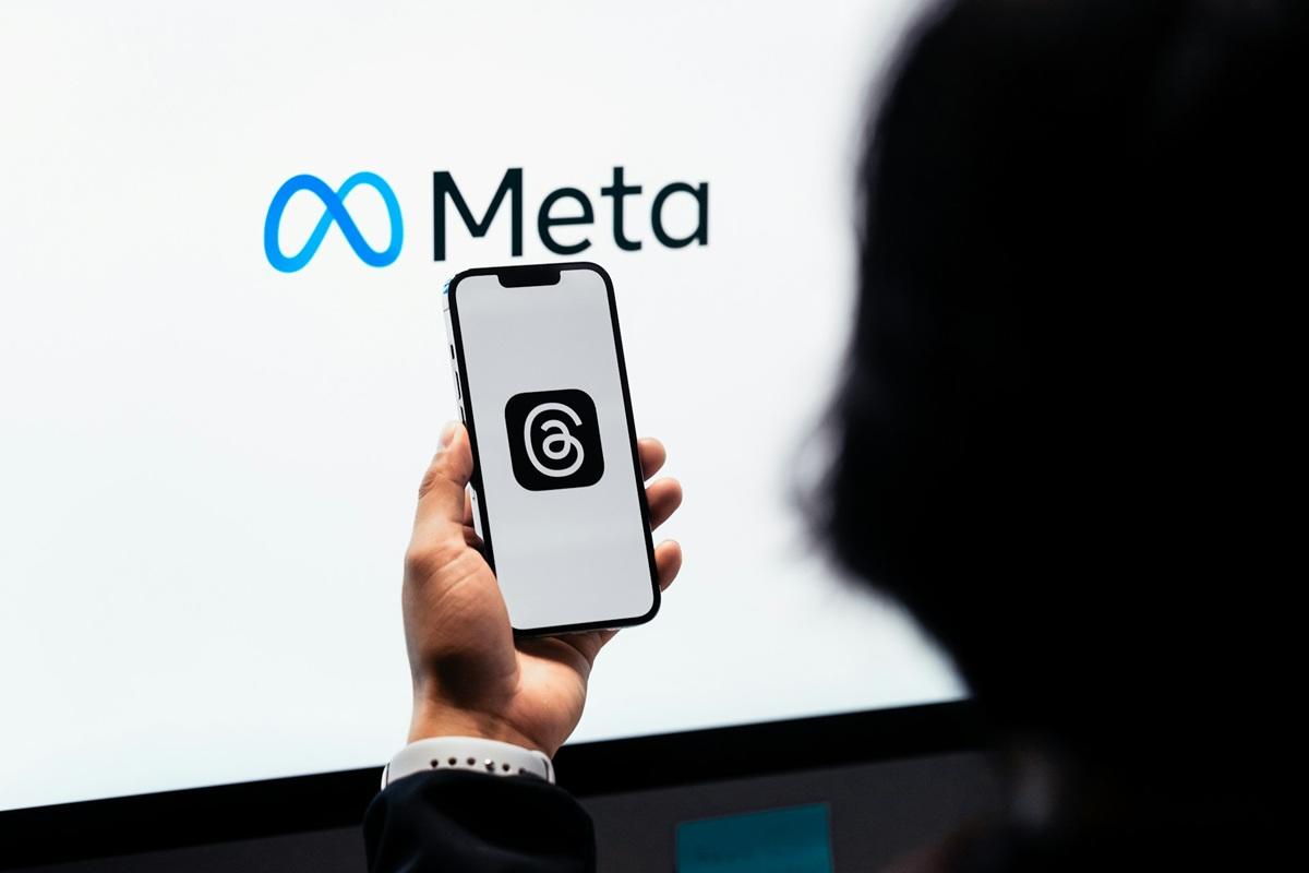 Une personne consultant l'application Threads sur son téléphone portable, avec le logo Meta en arrière-plan