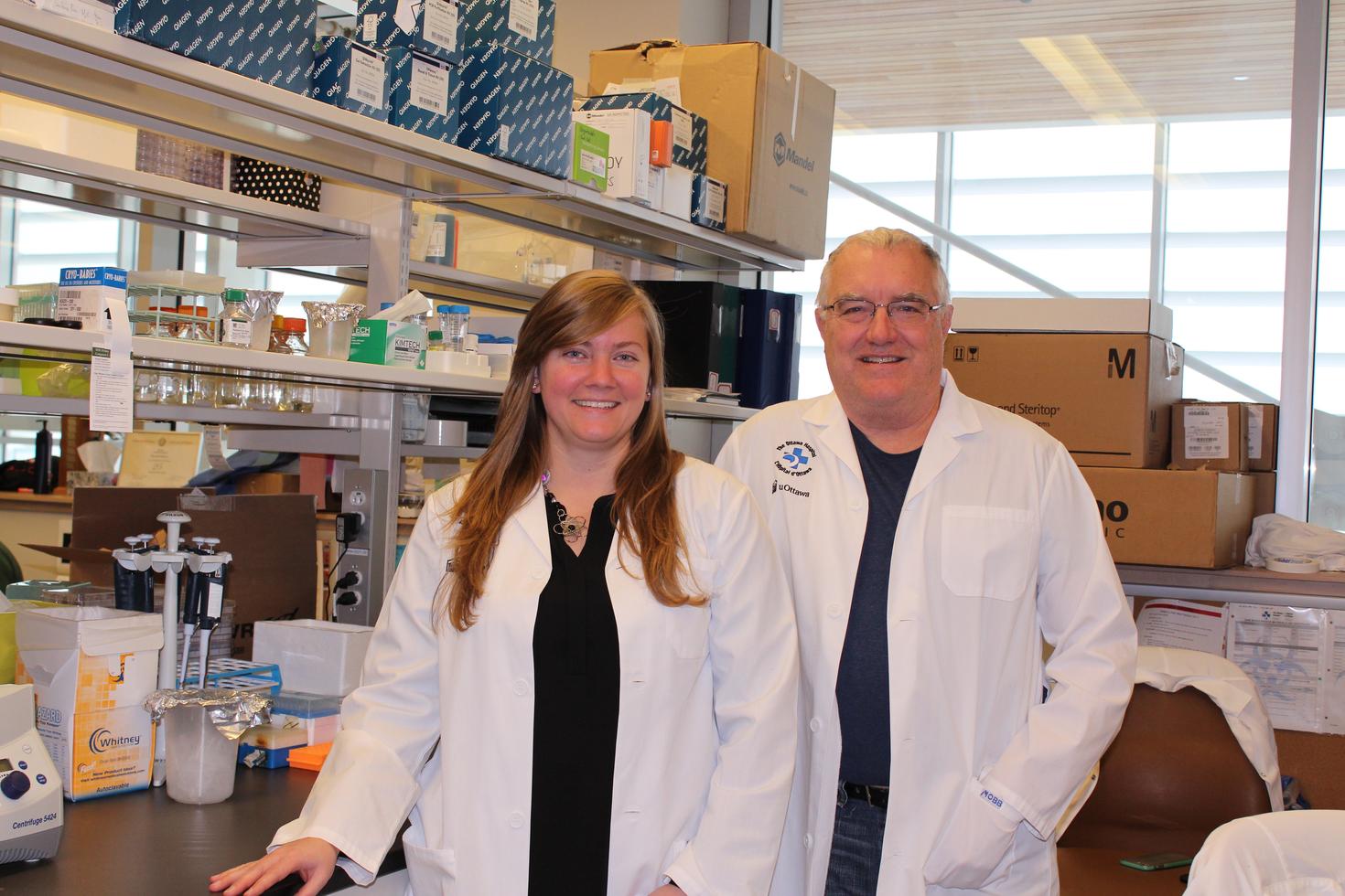 Une femme et un homme, en sarraus, sont debout dans un laboratoire de recherche.