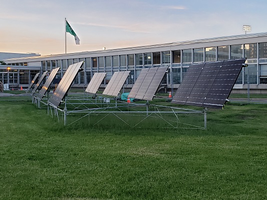 Image de huit panneaux photovoltaïques sur une pelouse à côté d’un bâtiment avec beaucoup de fenêtres.