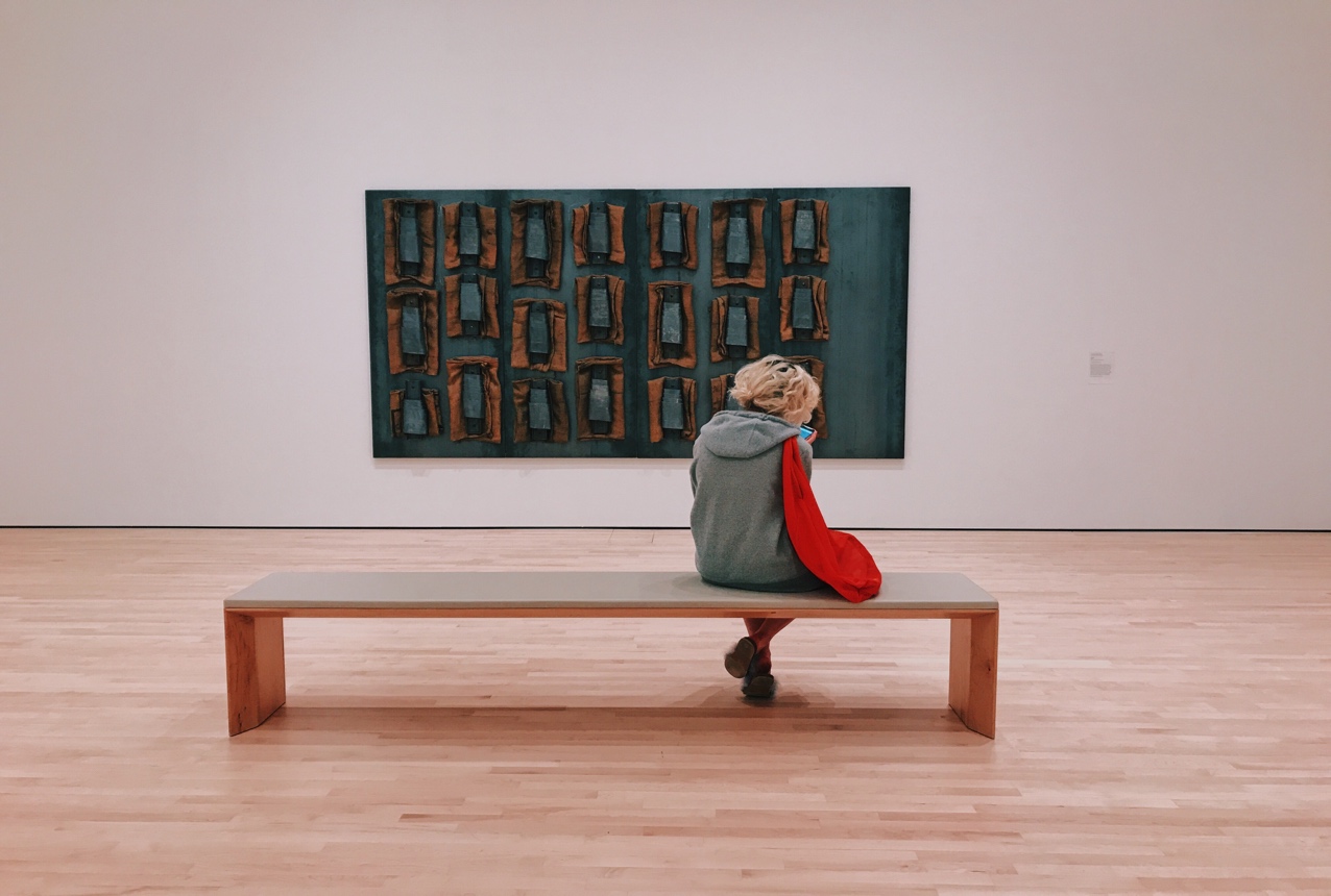 Une personne assise sur un banc dans une gallerie d'art.