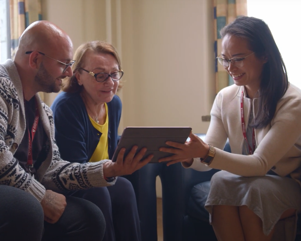 La Dre Amy Hsu souriant et montrant de l’information sur un iPad à une femme et à son fils adulte.