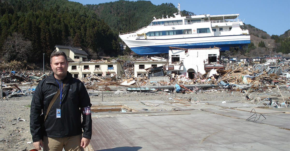 Le professeur Ioan Nistor se tient devant un bâtiment et un navire ravagés par le tsunami survenu en 2011 dans la région de Tohoku au Japon.