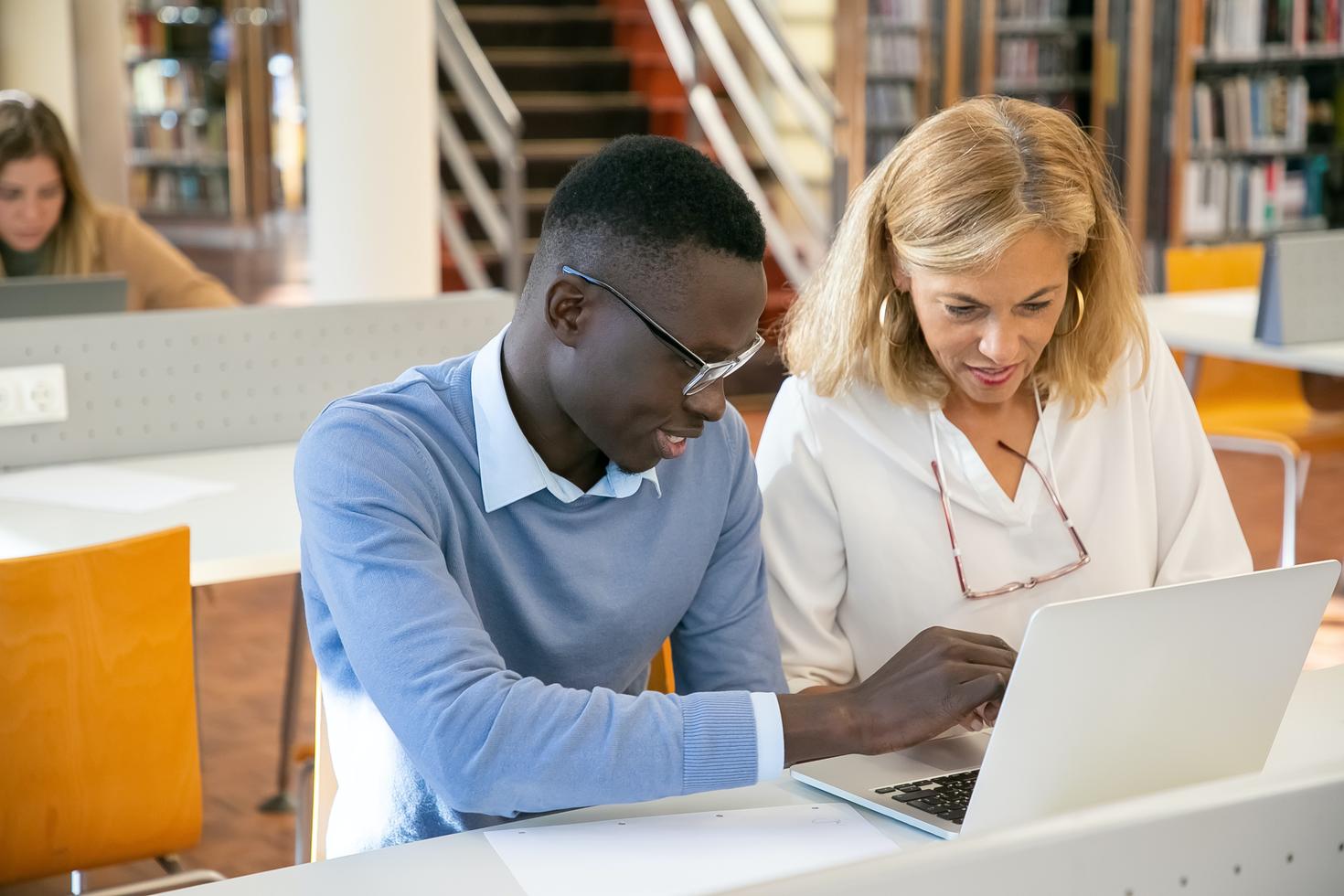 Un enseignant aide un étudiant qui travaille sur son ordinateur portable à la bibliothèque