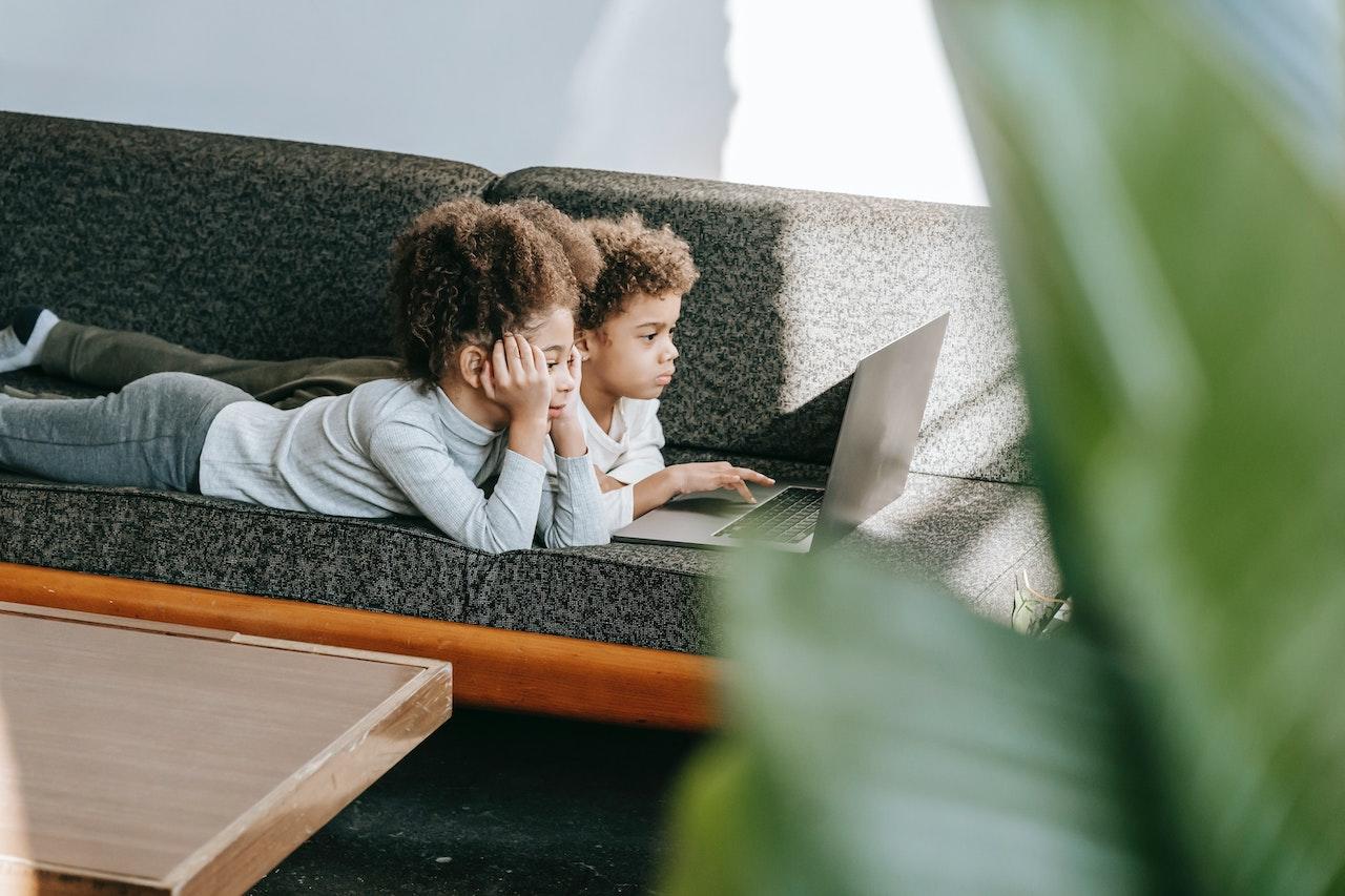 Deux enfants sur un canapé regardant un écran d'ordinateur