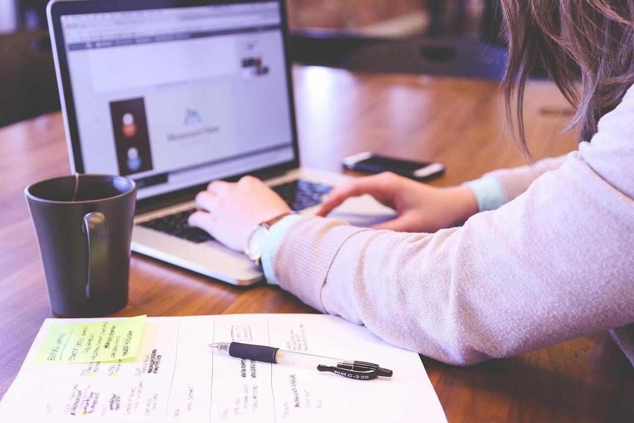 Femme tapant sur le clavier d'un ordinateur portable avec un carnet de notes et une tasse de café.