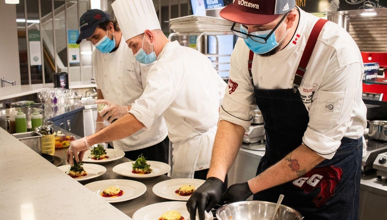 Des chefs préparent des plats dans la salle à manger du Centre Universitaire Jock-Turcot (UCU) de l'Université d'Ottawa.