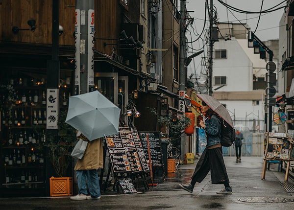 Pedestrians with umbrellas walking down city street in rain.