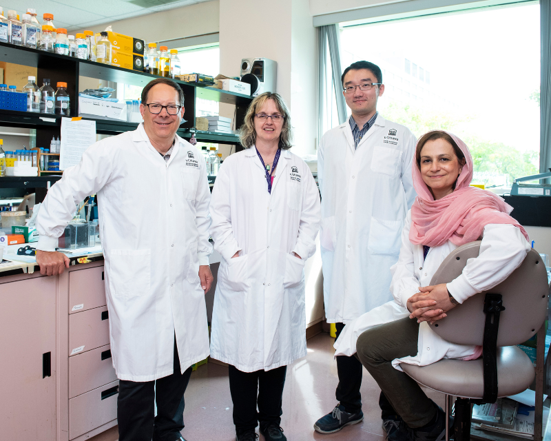 Dr. Paul Albert standing and smiling with his lab members. 
