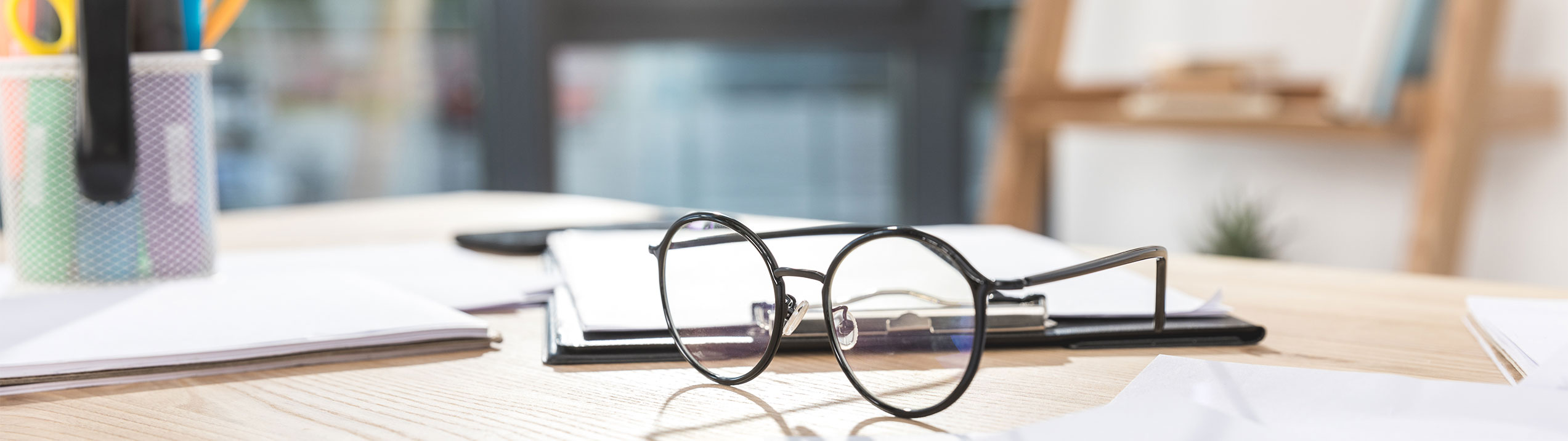 A pair of glasses resting with a notebook on a wooden table.