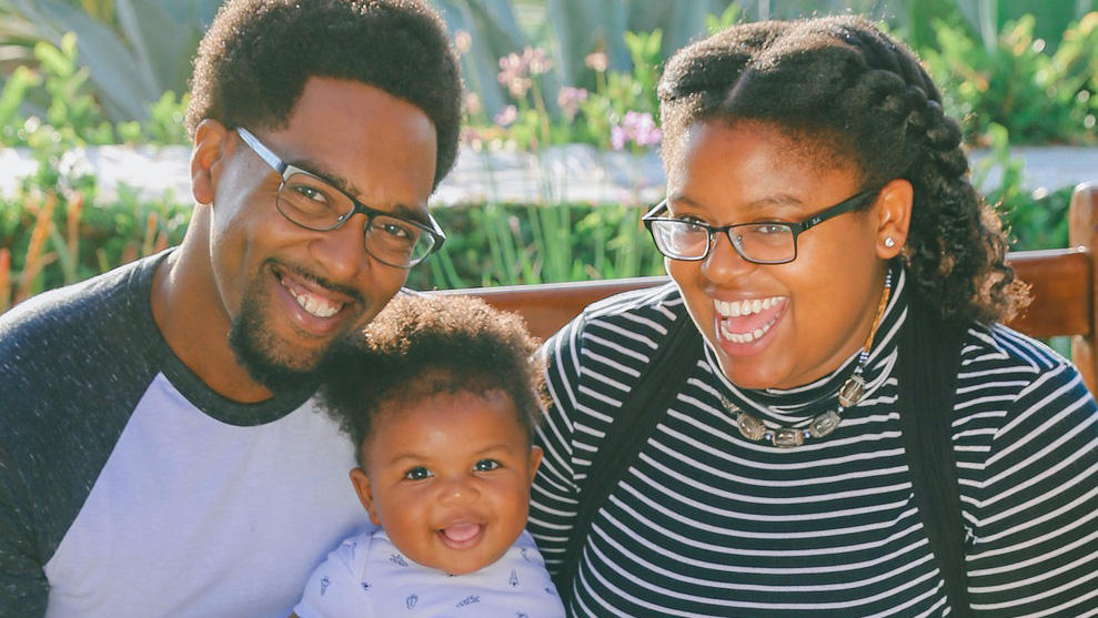 A family made of a father, a mother and a baby is smiling.