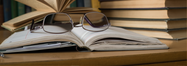 Book stack on the side, and eyeglass on an open book in the center.