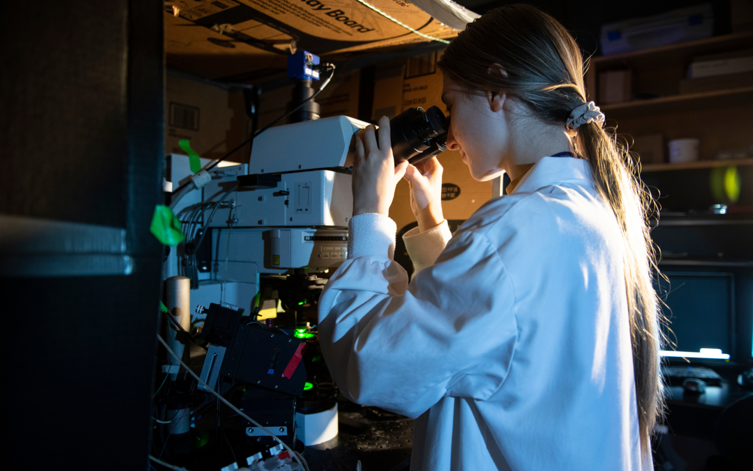 Researcher using microscope in dark room.