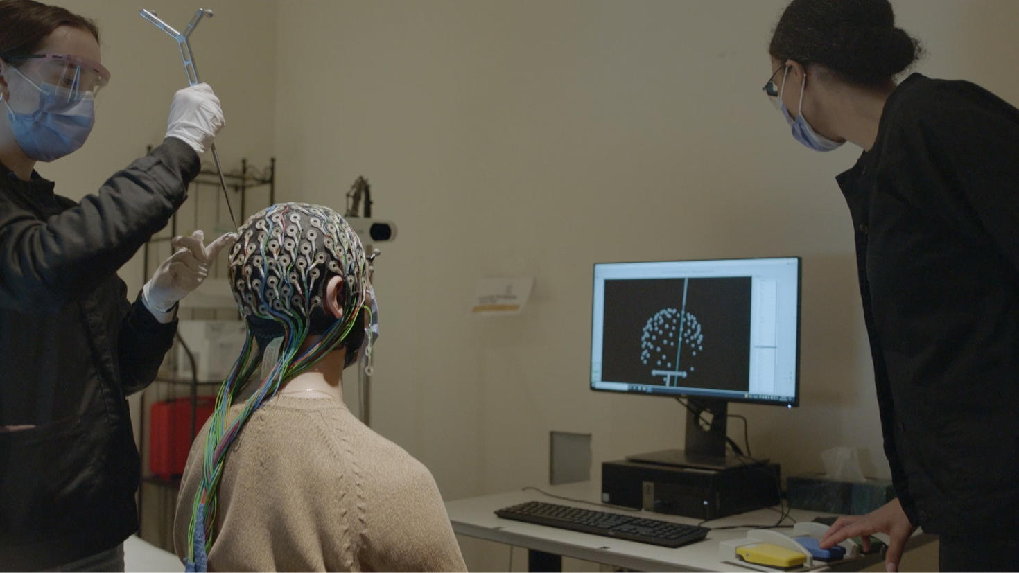 EEG experiment in a lab, with researchers adjusting electrodes and data displayed on a monitor.