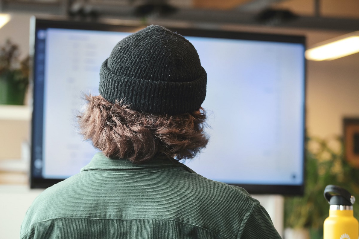 View from behind of man in toque looking at computer screen
