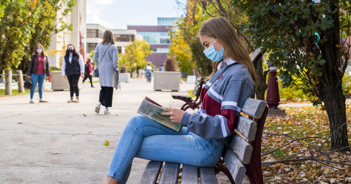 Une étudiante lit un livre à l'extérieur sur le campus.