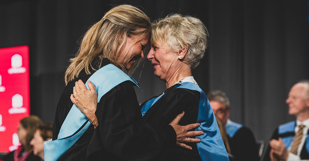 Deux femmes portant la toge se font une accolade lors de la collation des grades.