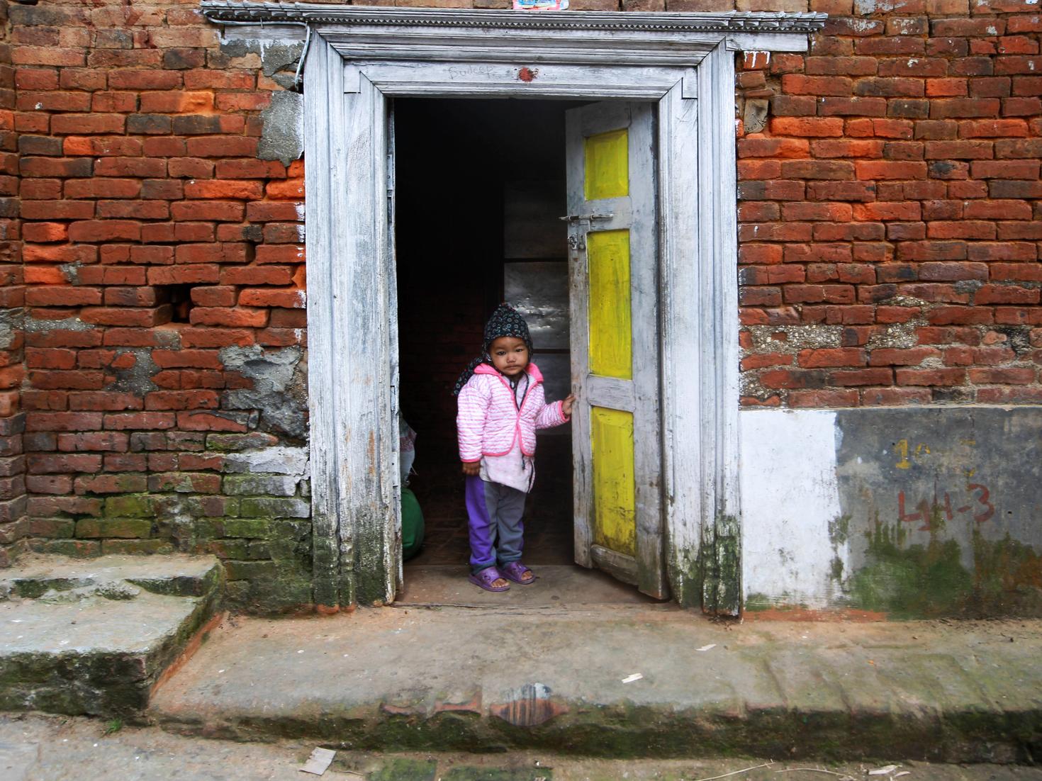 Un enfant ayant ouvert la porte principale du batiment. Mur orange ainsi que passage piéton en face de lui