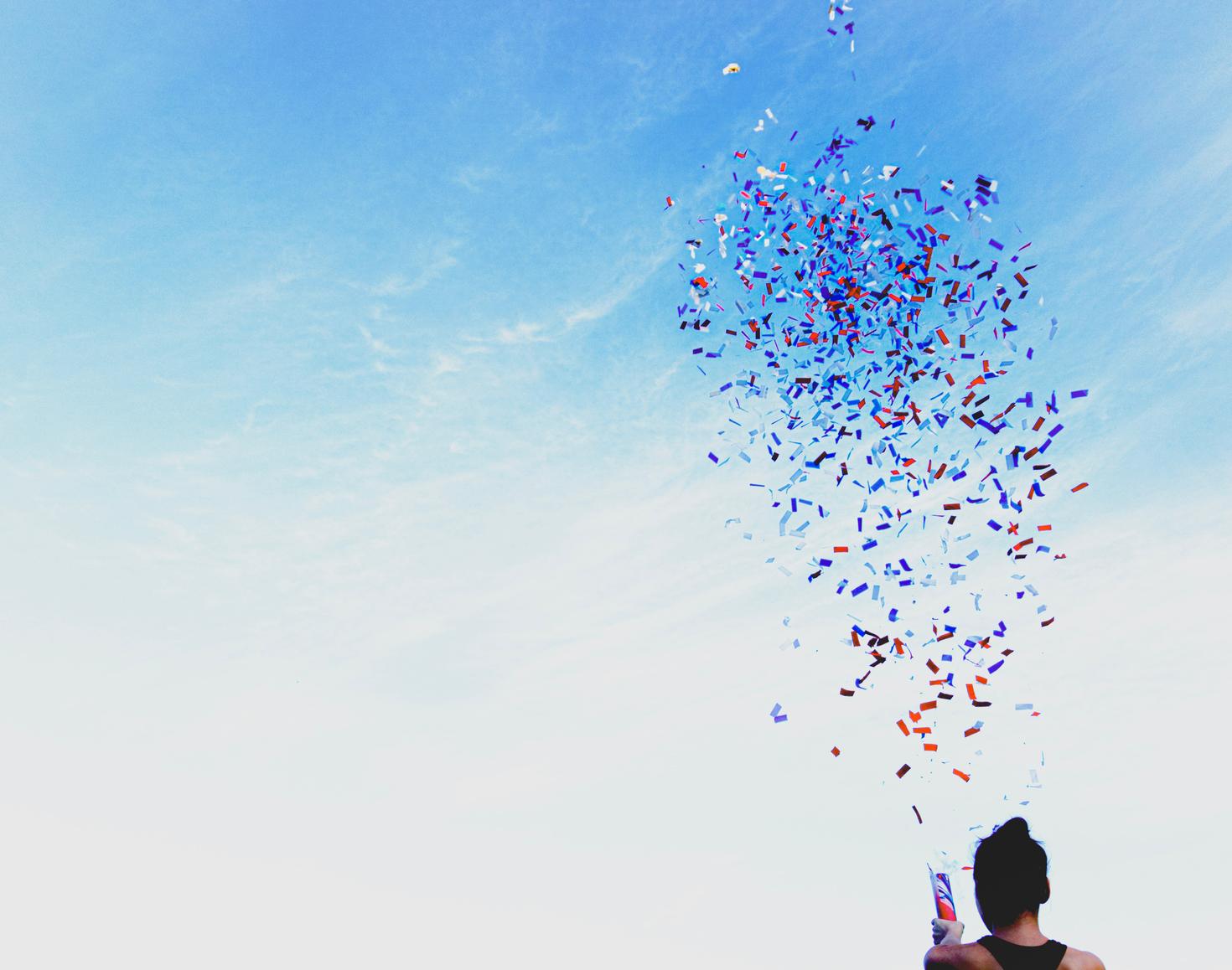 Silhouette setting off confetti in the blue sky
