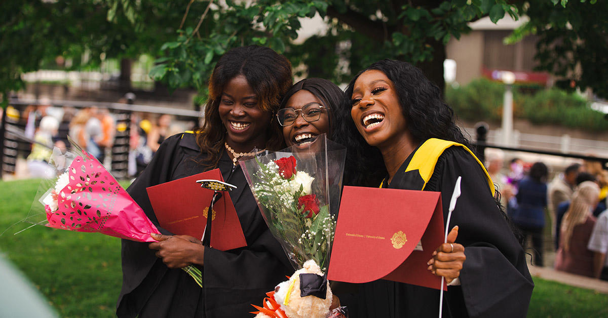 three graduates of faculty science smiling and laughing while holding their diplomas 