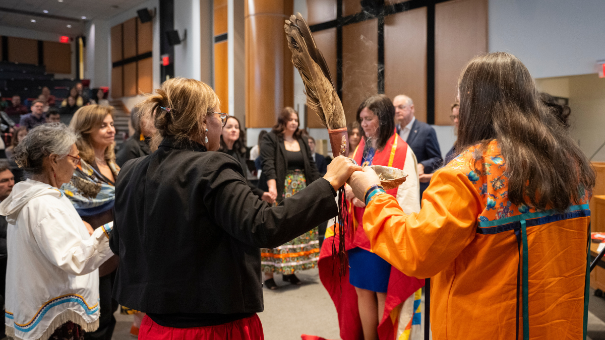 A woman stands in the centre of a circle of people. She is wrapped in a blanket. 