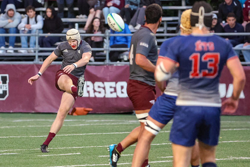 A Gee-Gees rugby player kicks the ball towards opposing players during a game.