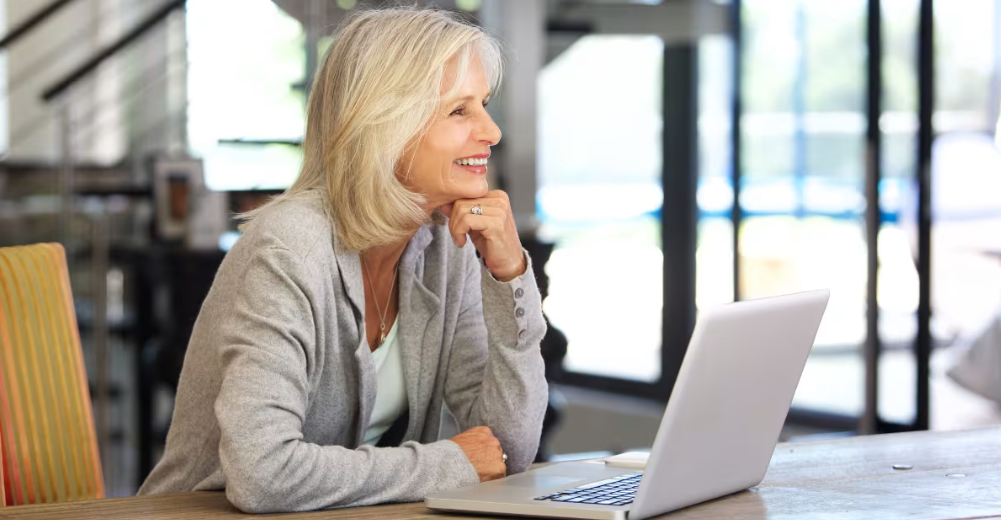 Femme souriante assise à une table et regardant l'écran d'un ordinateur portable.