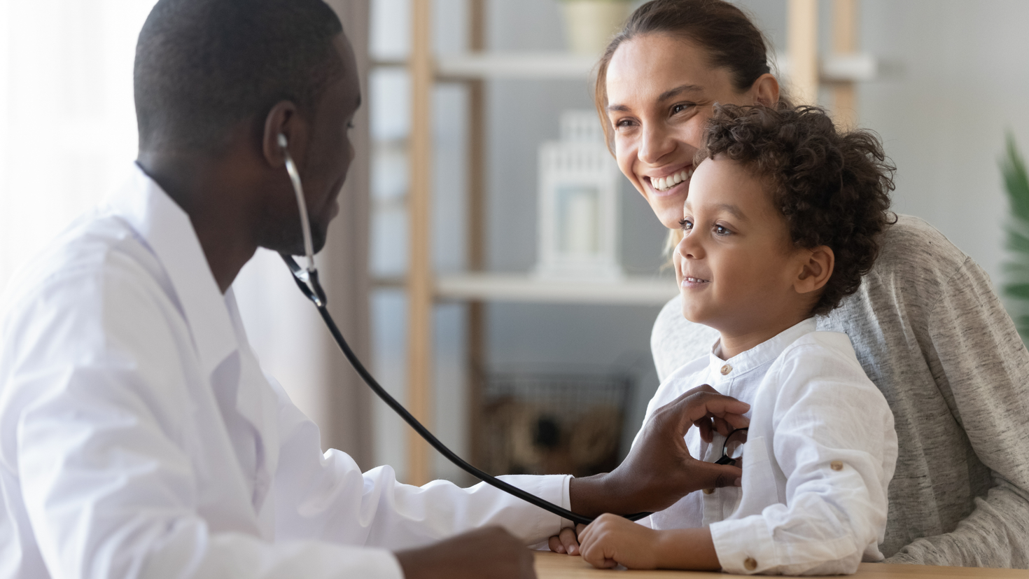 A doctor uses a stethoscope to check a child's heartbeat with his mother looking on