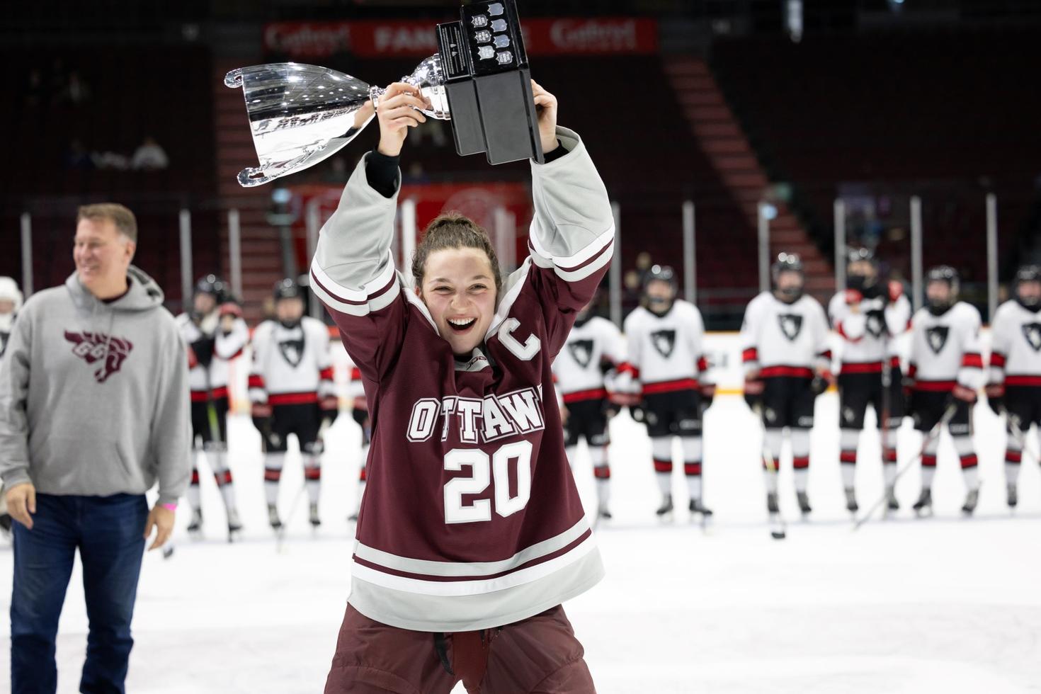 A player on the women's Gee Gees hockey team raises the Alerts Cup trophy in the air.