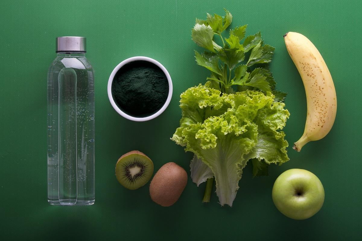 A bottle of water, a kiwi, lettuce, an apple, a banana and more on a green background