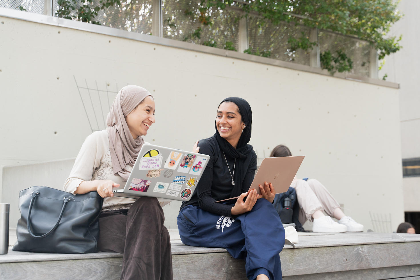 Deux étudiants, assis dehors sur le campus avec leur ordinateur portable, en train de rire