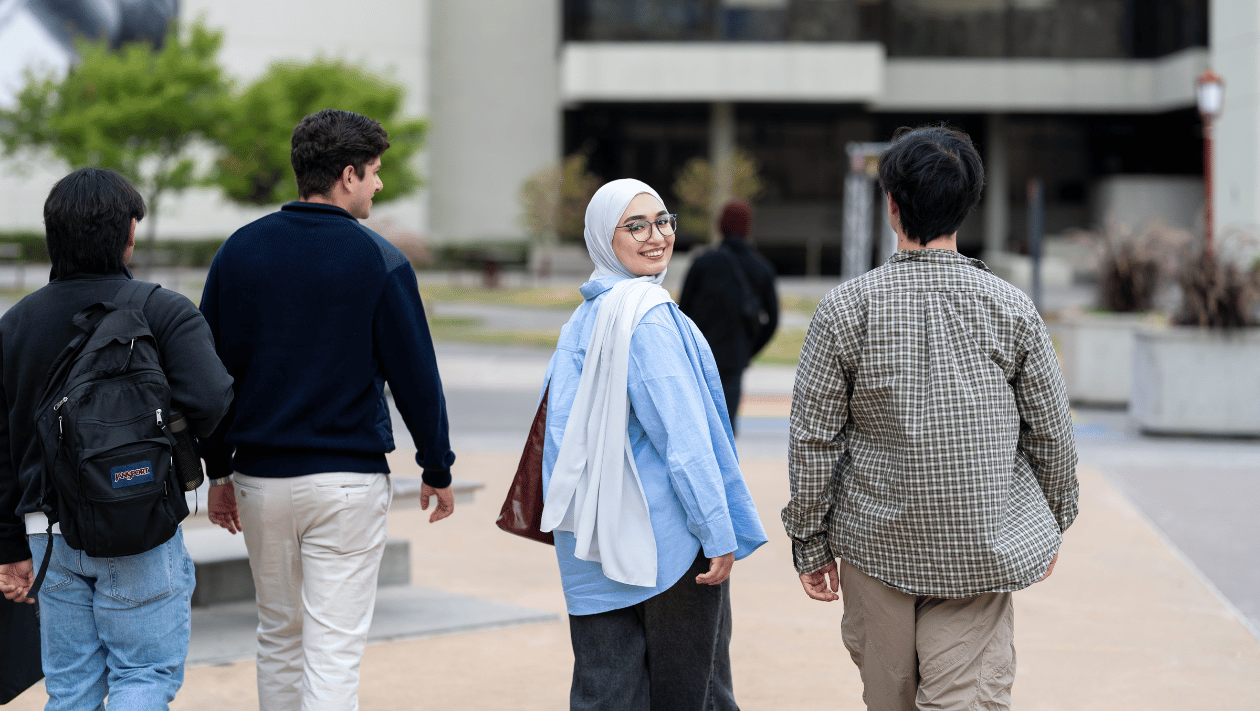 Four students walking on campus. One of them is looking back at the camera.