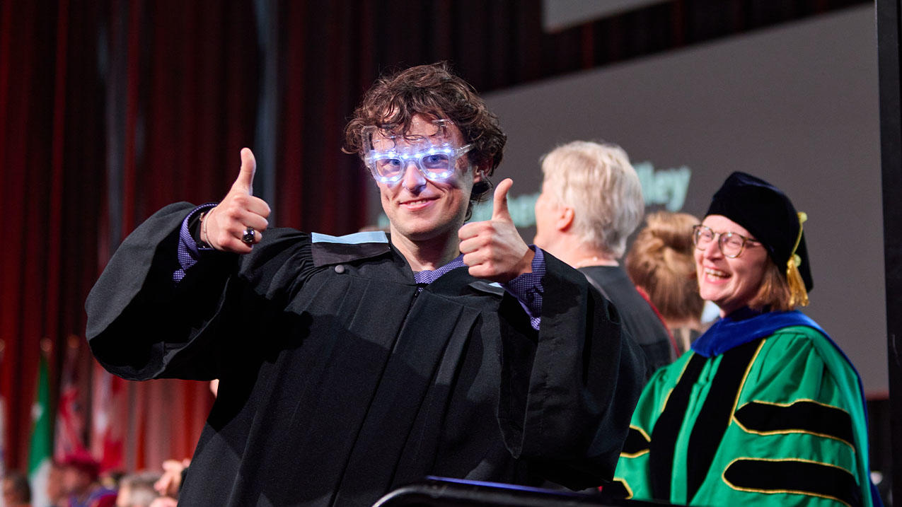 Graduate in sparkling glasses giving thumbs up