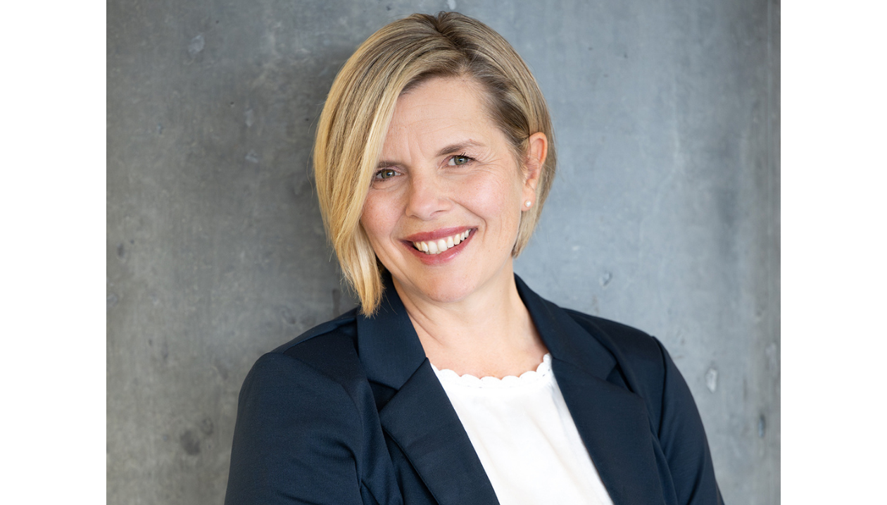 Portrait professionnel de la professeure Stéphanie Gaudet, souriante, portant un veston bleu marine devant un fond gris.