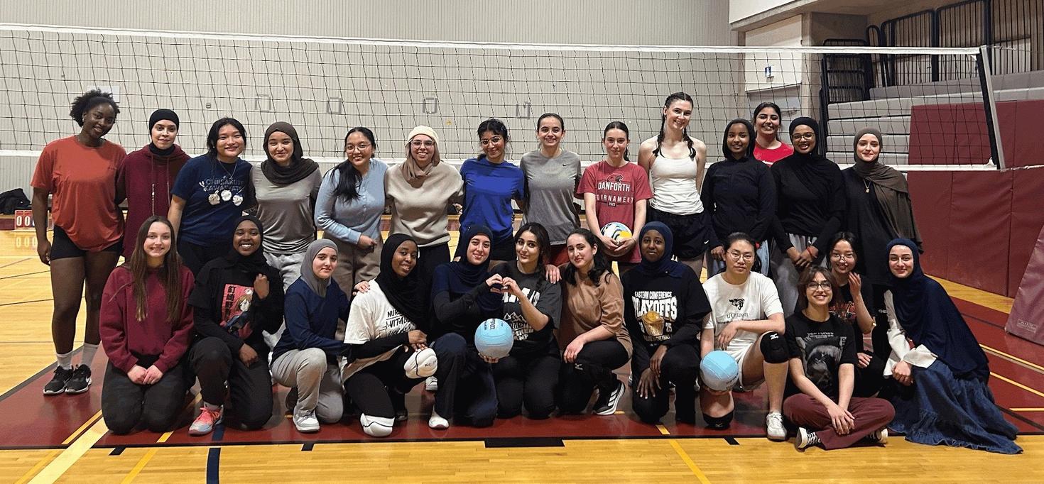More than 20 members of uOttawa WeSport pose in a group in a gym in front of a volleyball net.