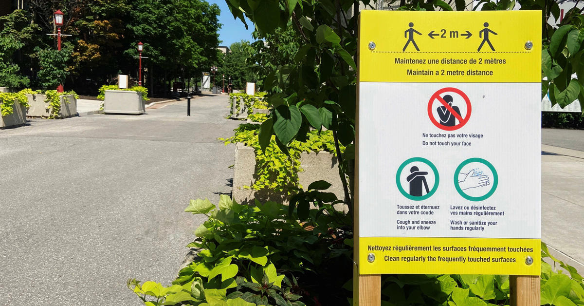 A pedestrian street on campus with an outdoor sign with instructions to prevent the spread of the virus