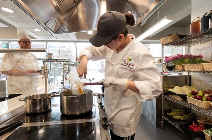 Une femme verse de la sauce dans un chaudron sous les yeux d'un chef.