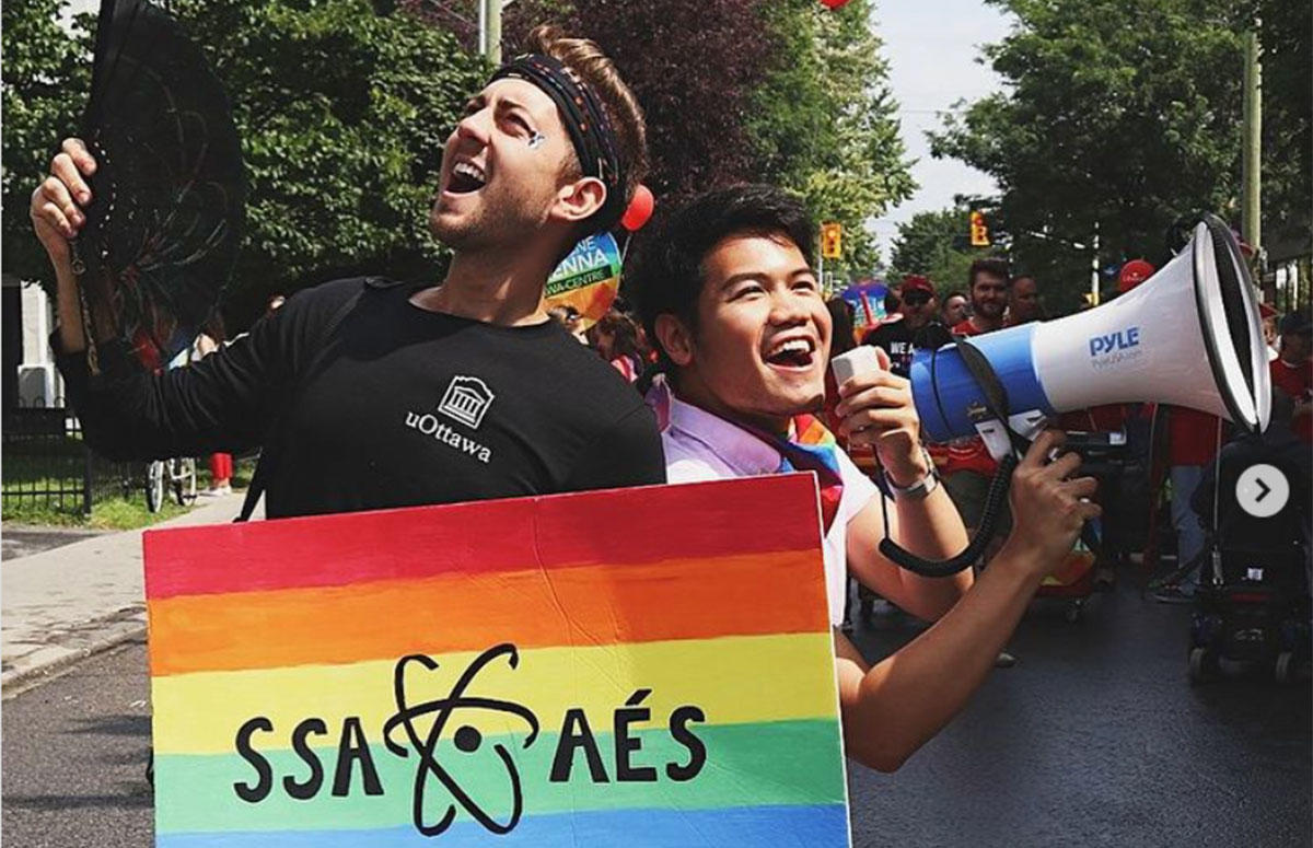 Jesse Lesniowski et Dasa Soekotjo tenant un panneau avec l'arc-en-ciel de la fierté gaie et le logo de l'Association des étudiants en sciences