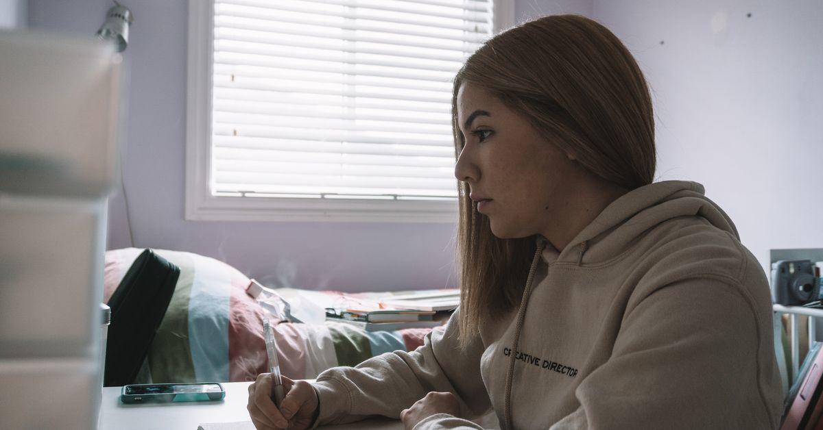 Une jeune femme vue de profil est assise devant son ordinateur portable.