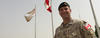 Dr. Maxime Britt-Côté standing in front of flags wearing a beige camouflage uniform.