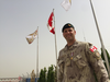 Dr. Maxime Britt-Côté standing in front of flags wearing a beige camouflage uniform.