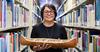 Eva Ottawa stands between shelves of books in the library, holding a canoe.