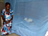 African woman sitting on bed draped in netting, where baby sleeps protected from mosquitoes.