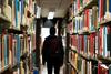 View of a person from behind between two rows of books in a library.