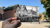 Alumni Hall with a hand holding up an old image of what Alumni Hall looked like in the mid-1800s.