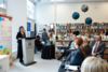 Lara Mainville standing at a podium speaking to a group of people.