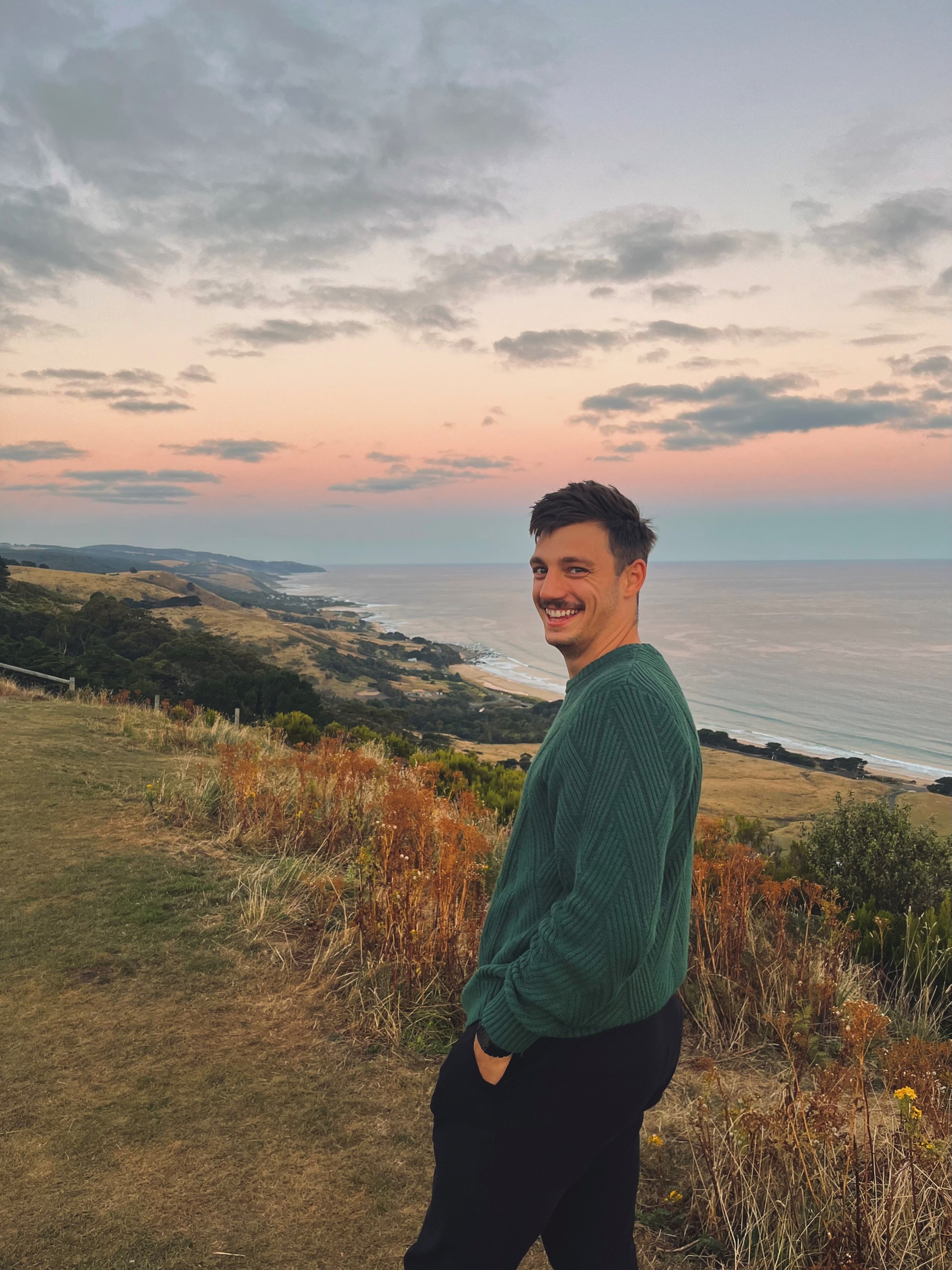 Young man standing in a green field in front of the sea