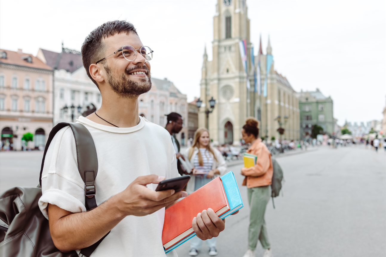 Young man with a set of books and a mobile phone smiling