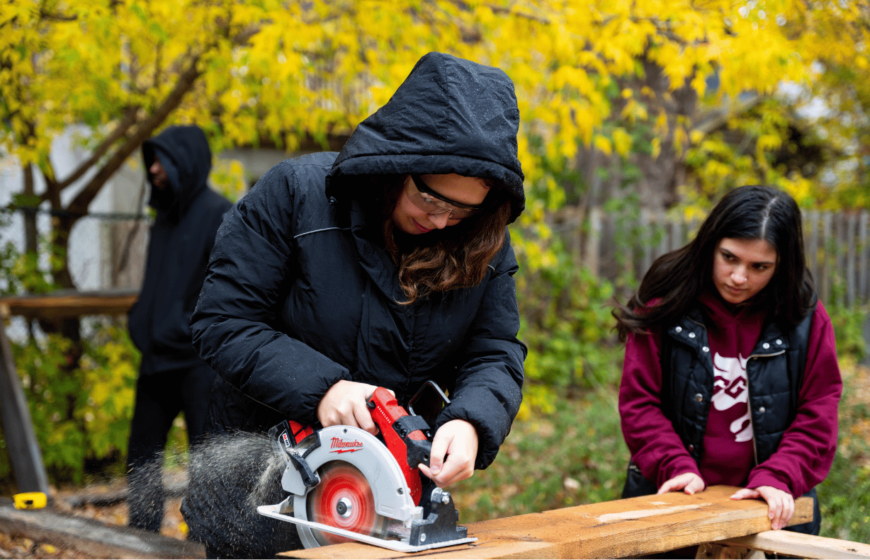 Two students cutting a piece of wood.