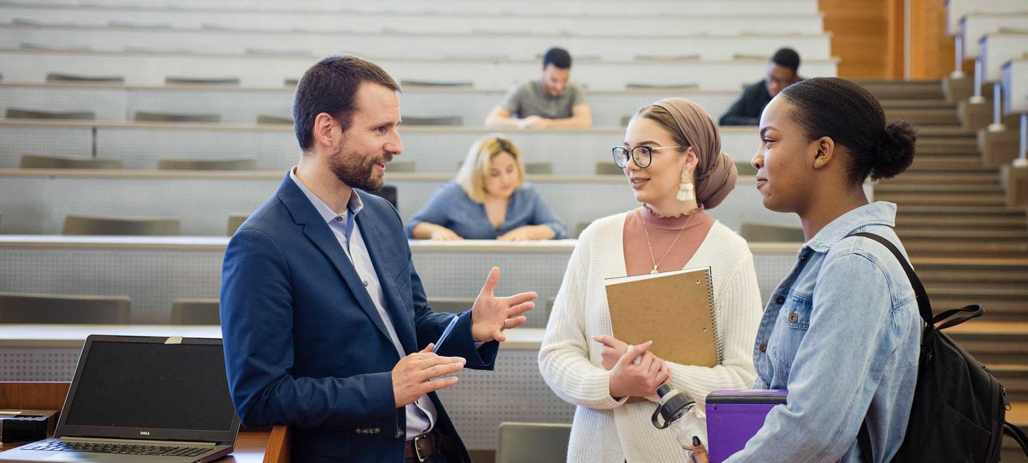 students talking to teacher at front of lecture hall