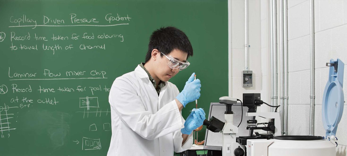 student in lab coat in lab using test tube and microscope